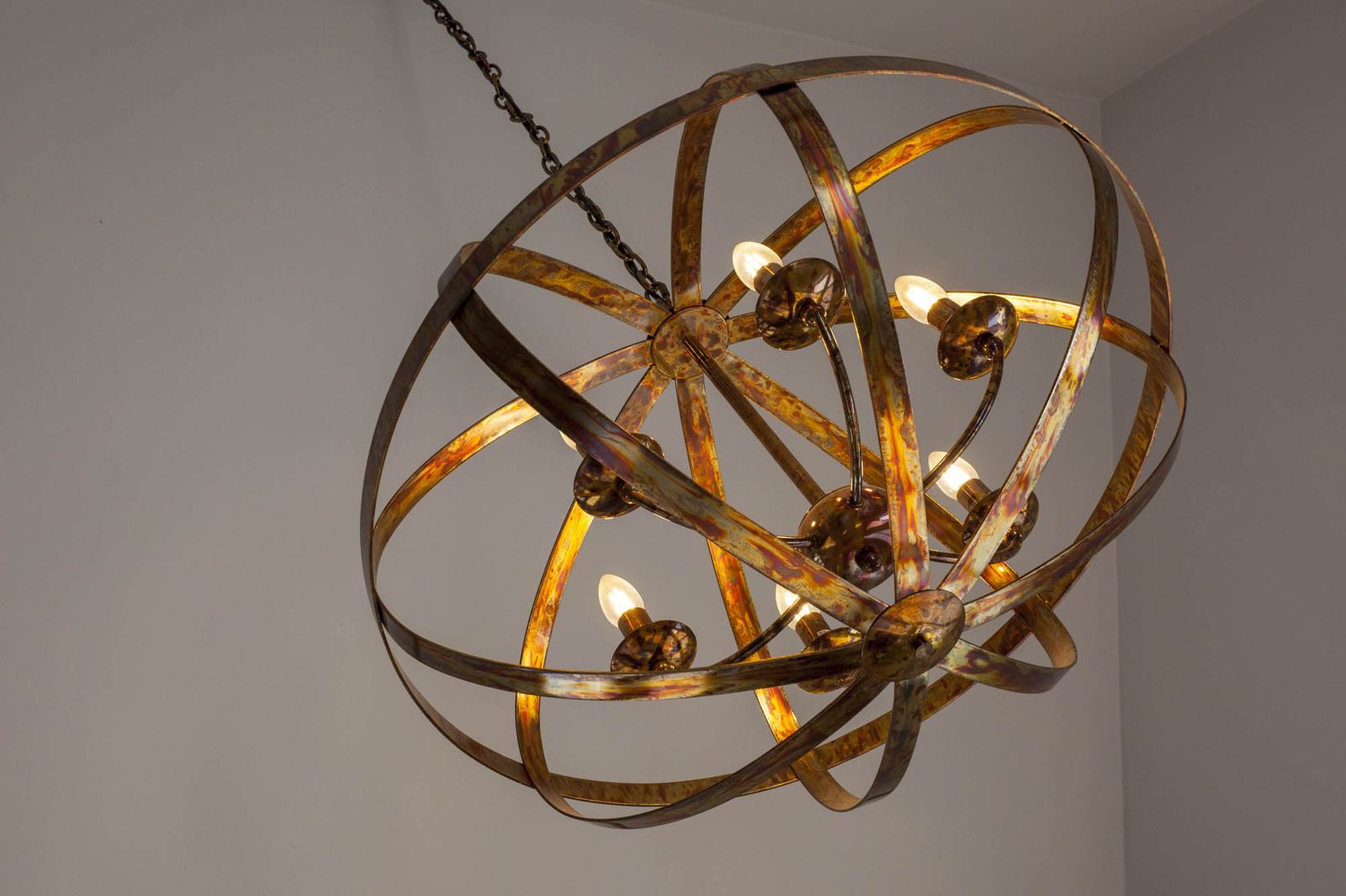 A brass orb chandelier with warm bulbs hanging against a pale wall in the barn